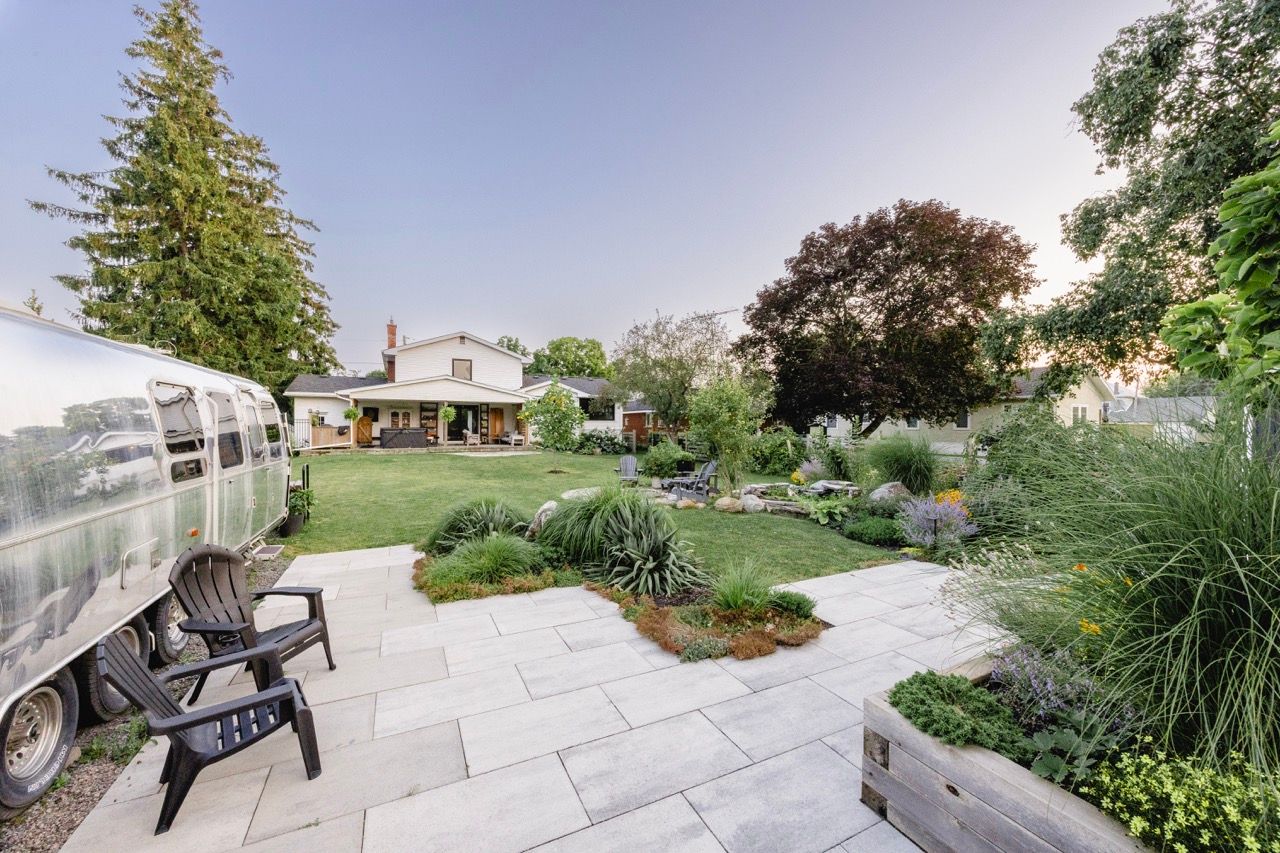Backyard patio featuring a vintage Airstream trailer, stone tiles, and beautifully landscaped gardens at twilight.