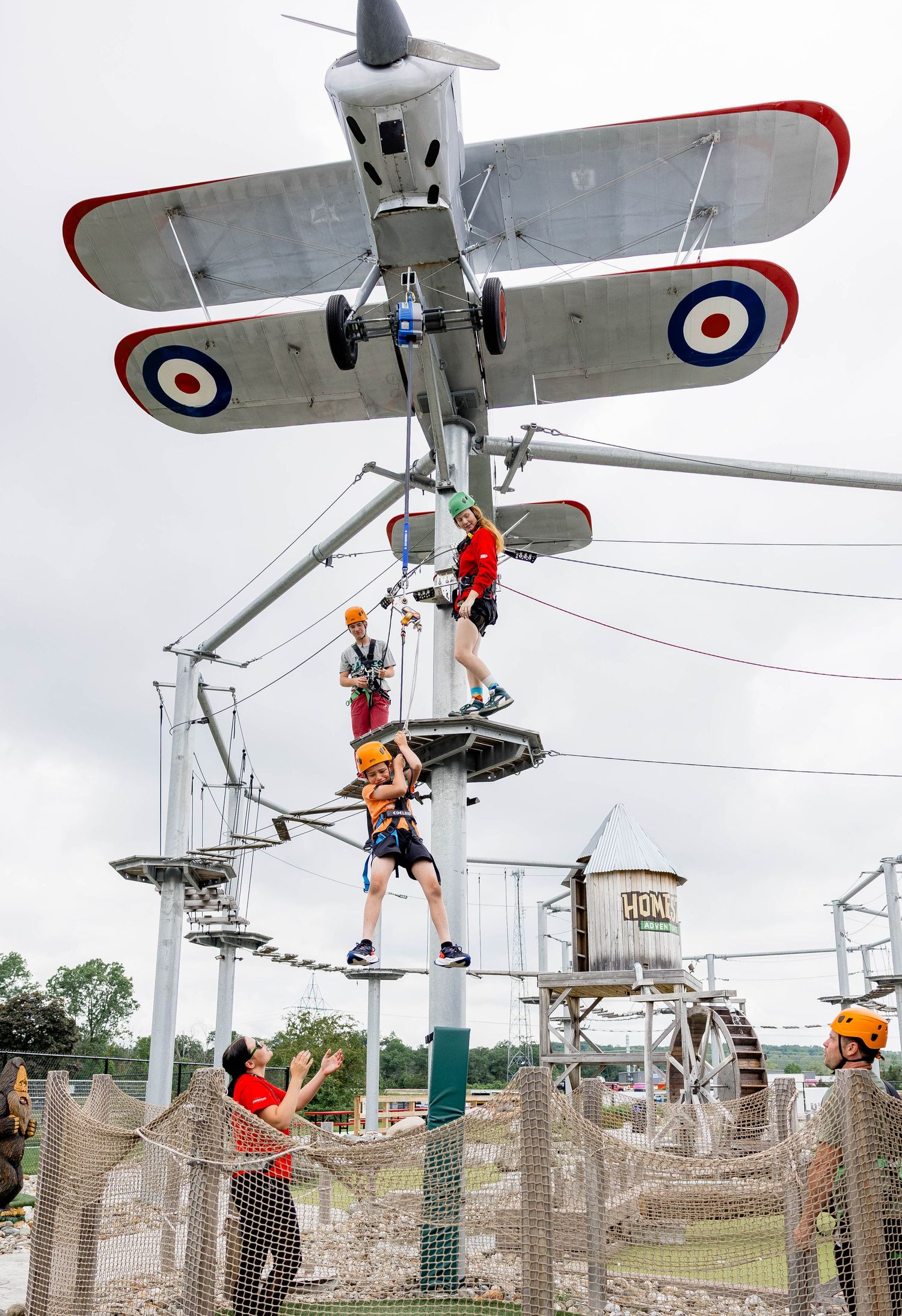 Group of children and adults navigating a high ropes adventure course with a vintage biplane centerpiece.