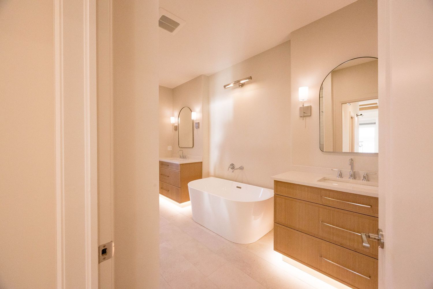 Elegant master bathroom with freestanding soaking tub, floating vanities, and warm ambient lighting.