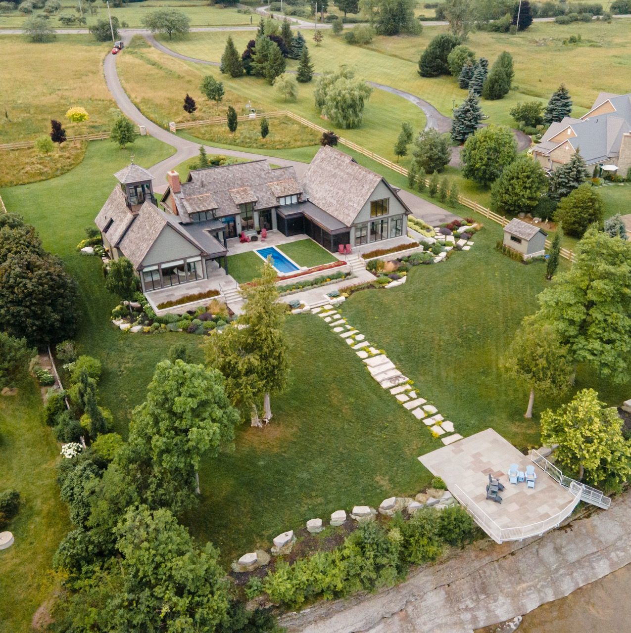 Bird's-eye view of a large country home with a swimming pool, stone pathways, and lush surrounding landscape.