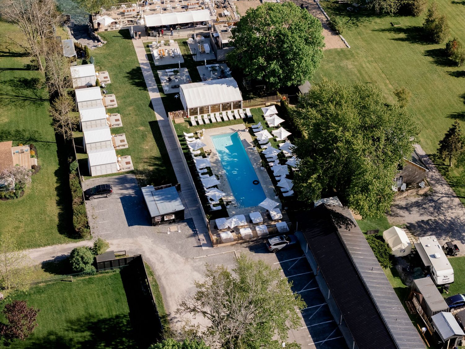 Aerial view of a resort with an outdoor pool, lounge chairs, and surrounding green landscape.