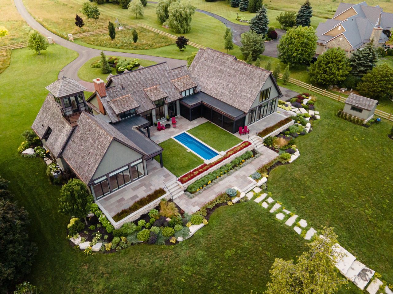 Aerial perspective of an elegant home featuring a rectangular pool, terraced gardens, and scenic countryside views.