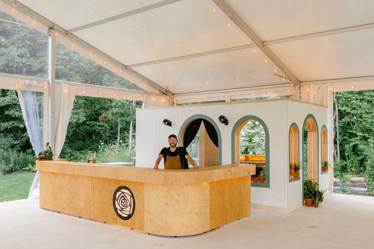 Elegant curved wooden bar inside a white tent venue with arched decorative backdrops.