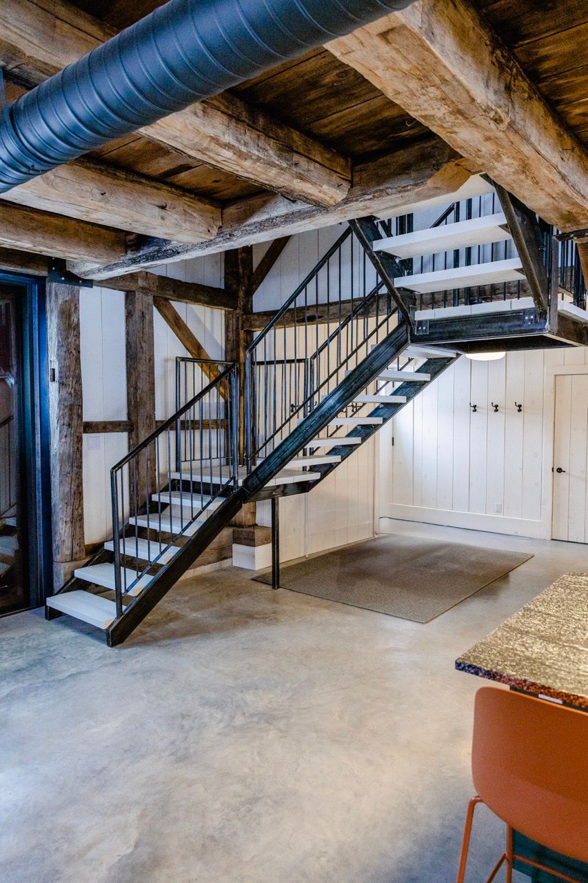 Industrial barn conversion staircase with black metal railings, exposed wood beams, and concrete floors.