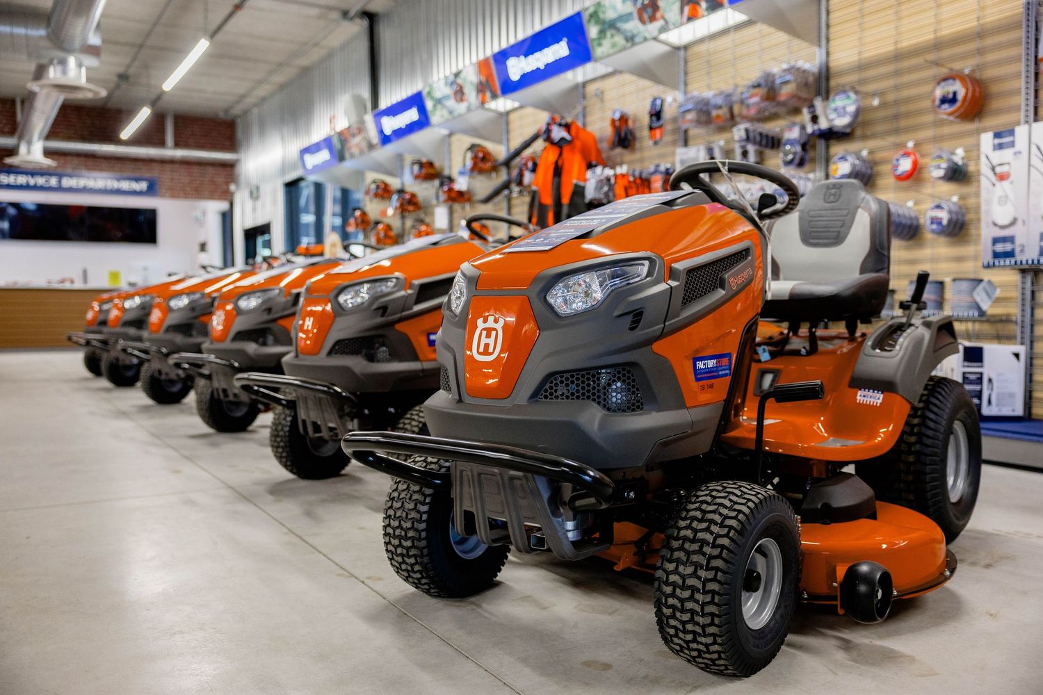Row of orange Husqvarna riding lawn mowers displayed inside a bright retail store showroom.