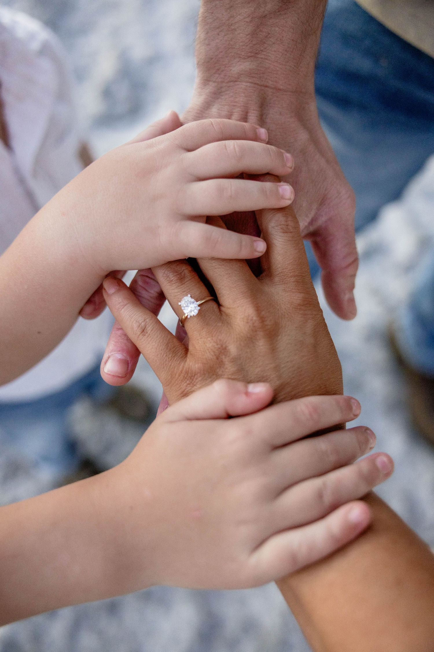 Close-up of family hands stacked together showing an engagement ring on woman's finger.