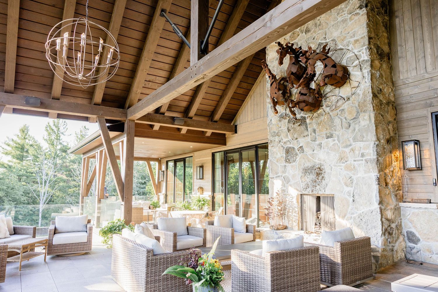 Rustic outdoor living space with timber beams, stone wall, wicker seating, and globe chandelier.