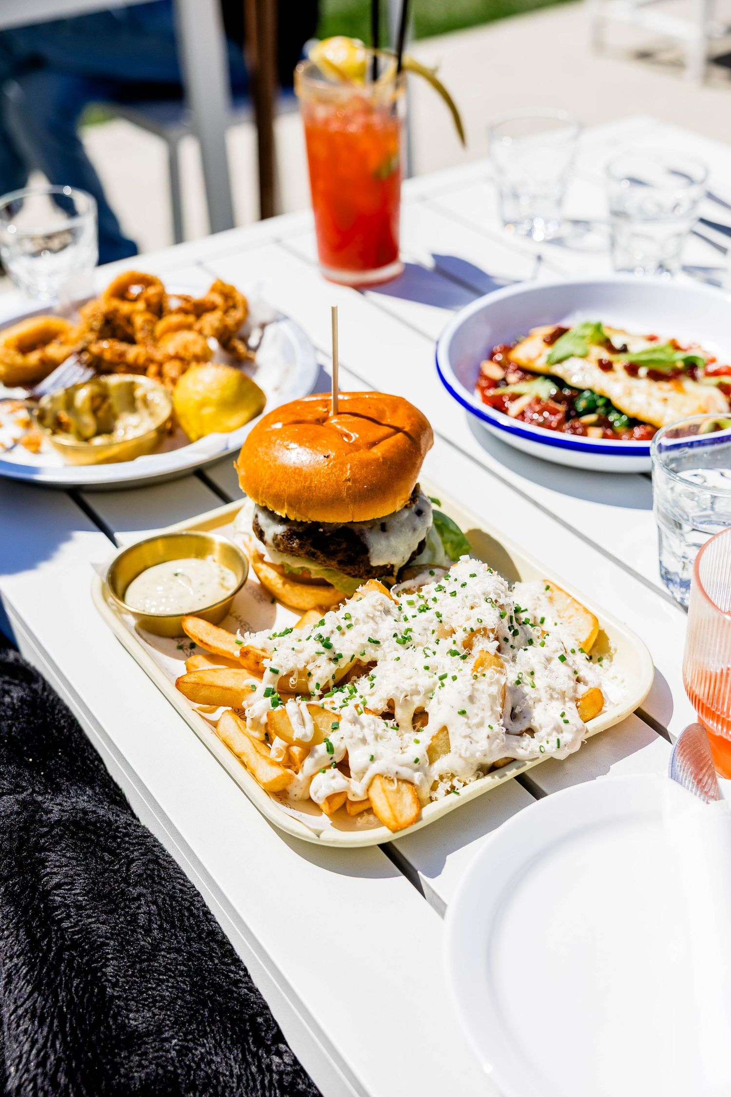 Gourmet burger with fries and coleslaw on white table with onion rings and salad in background.
