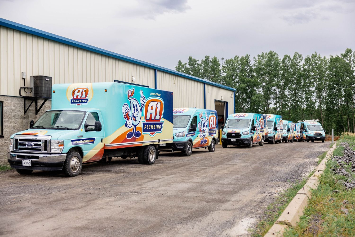 Fleet of colorful A1 Plumbing branded service vans lined up outside a commercial building.