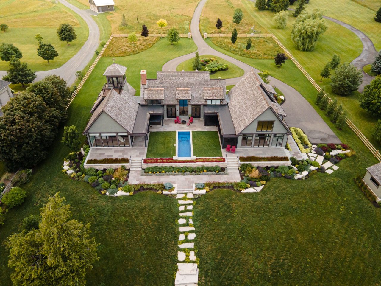 Aerial view of a luxury estate with a pool, manicured gardens, and expansive green lawns in a rural setting.