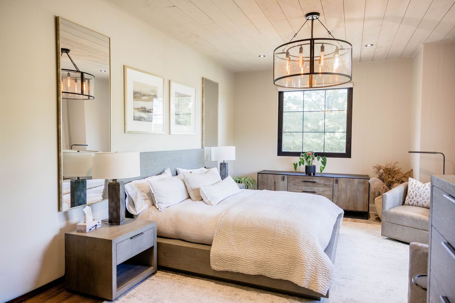 Elegant neutral bedroom with wood ceiling, pendant chandelier, upholstered bed, and natural light.