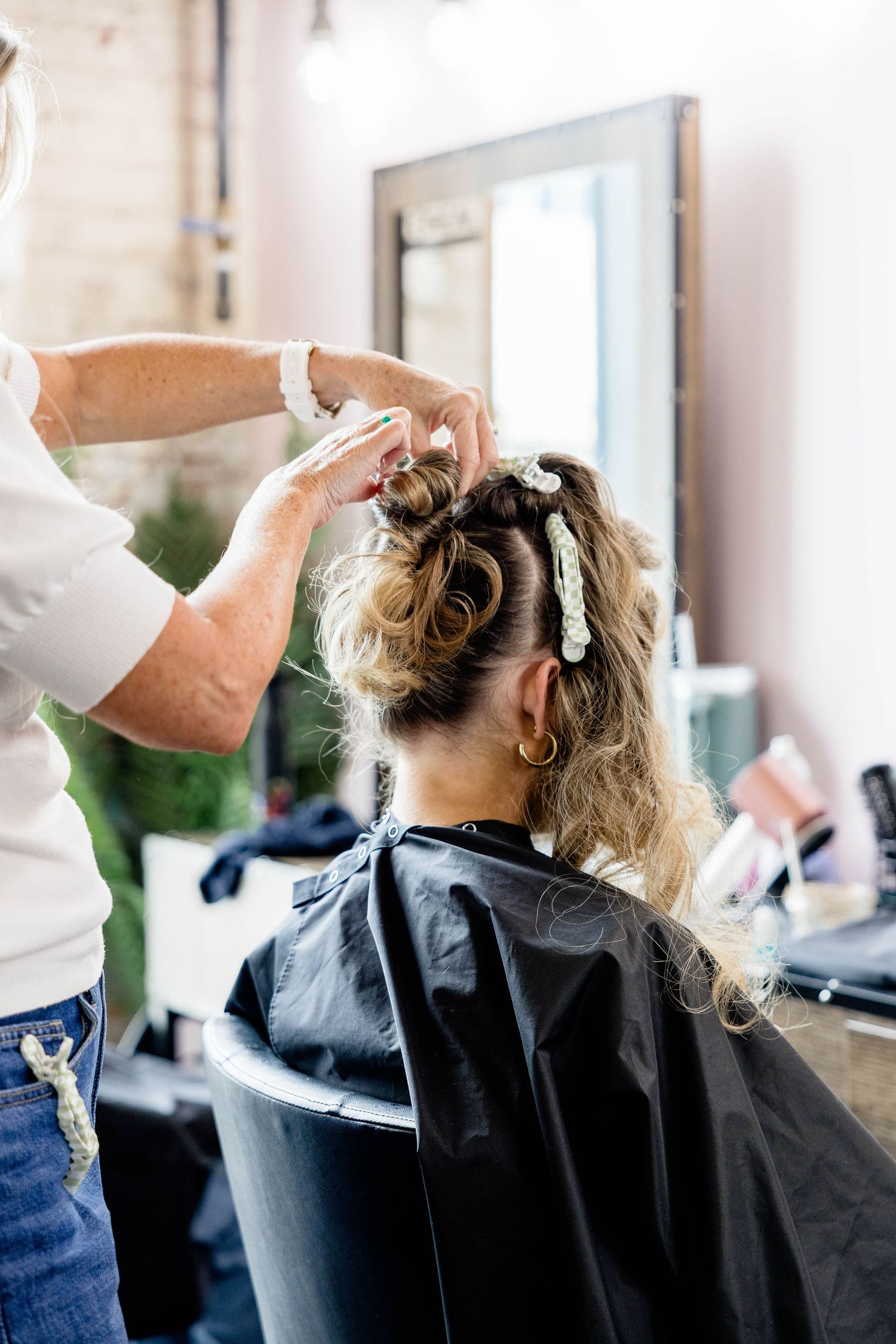 Hairstylist styling a blonde woman's updo with clips at a professional hair salon.