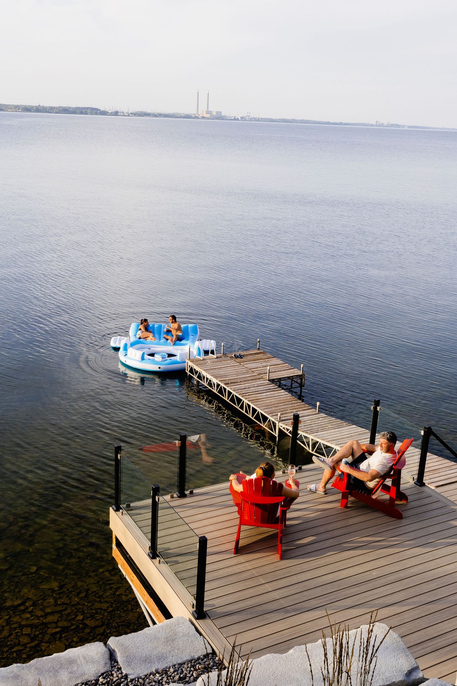 Group enjoying lakeside dock with red chairs while others paddle on blue pedal boat.