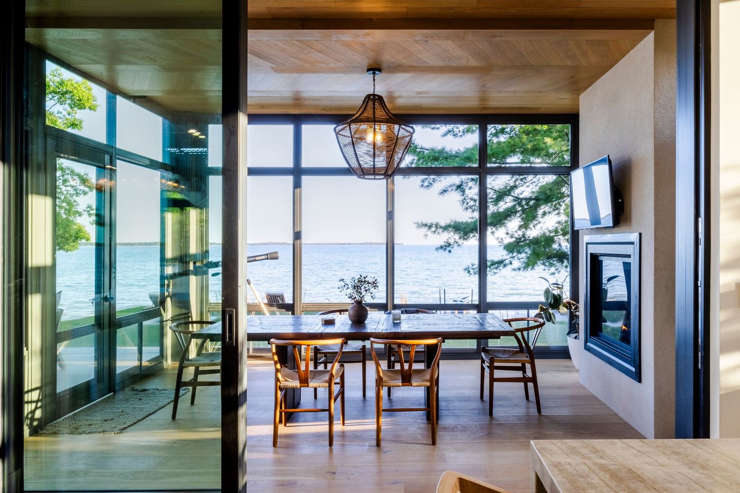 Dining room with floor-to-ceiling windows overlooking the ocean, wooden table, and modern fireplace.