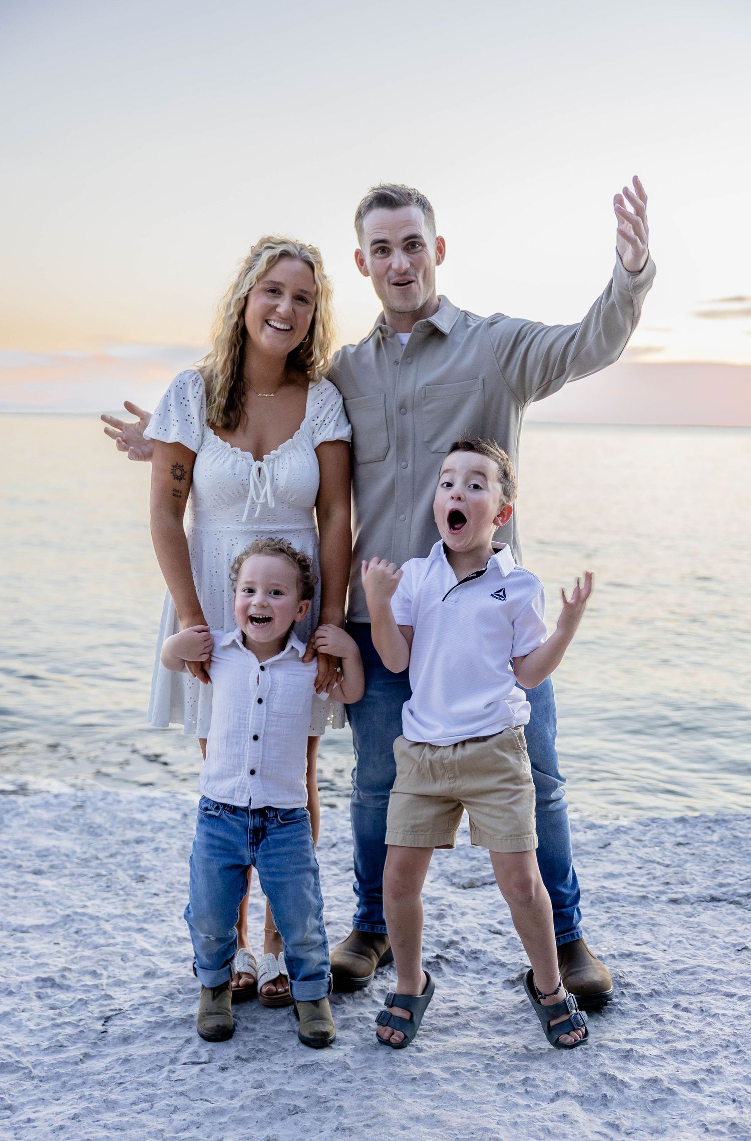 Joyful family of four posing playfully on beach at sunset with ocean backdrop.