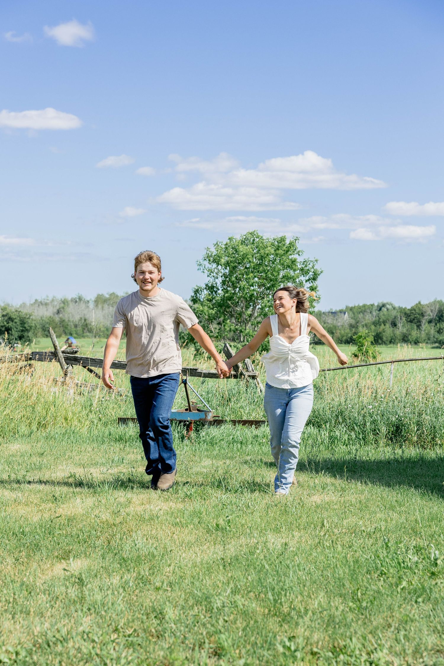 Happy couple holding hands and running together in a sunny green field on a beautiful summer day.