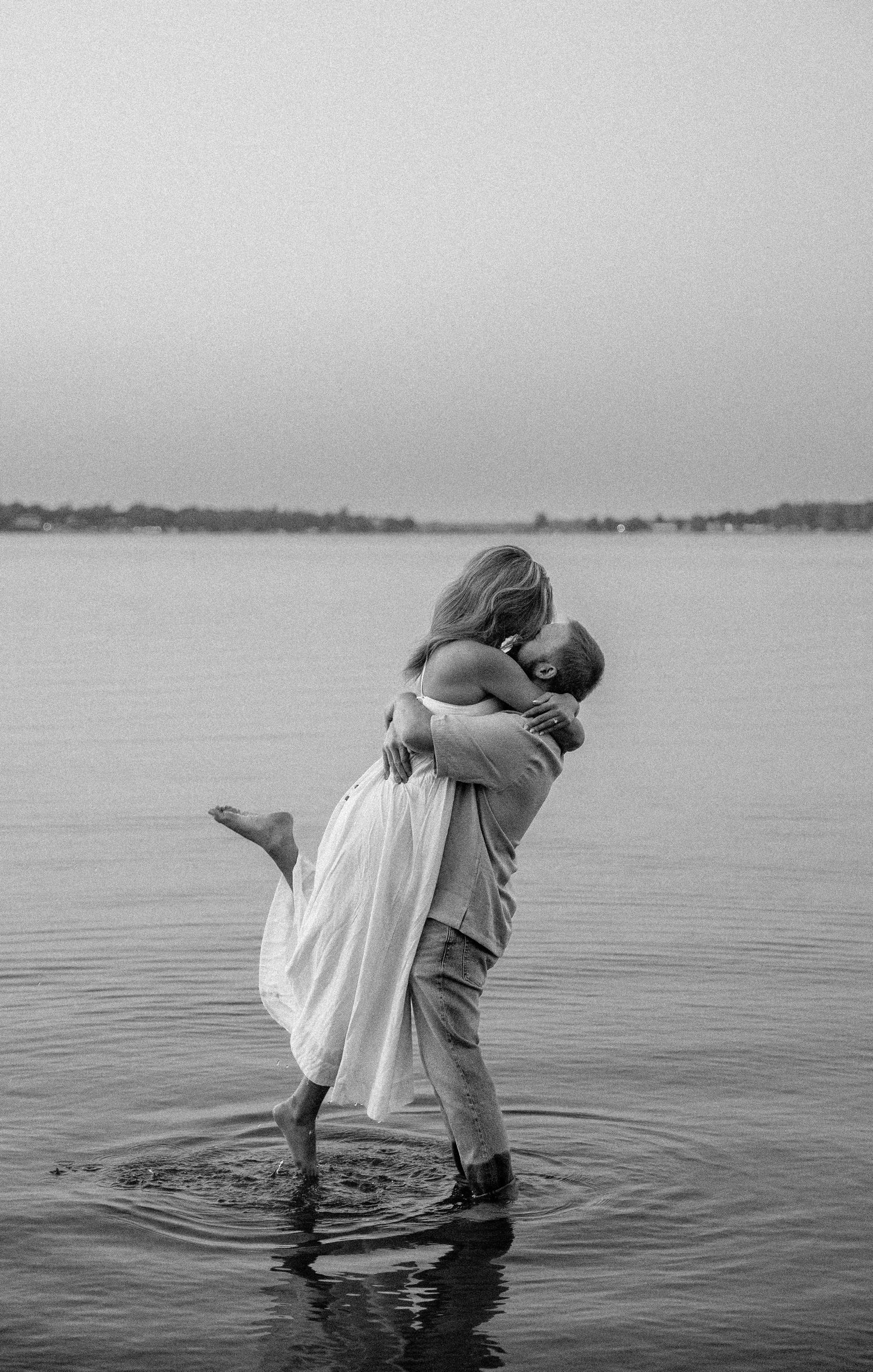 Black and white photo of couple embracing and kissing in lake water.