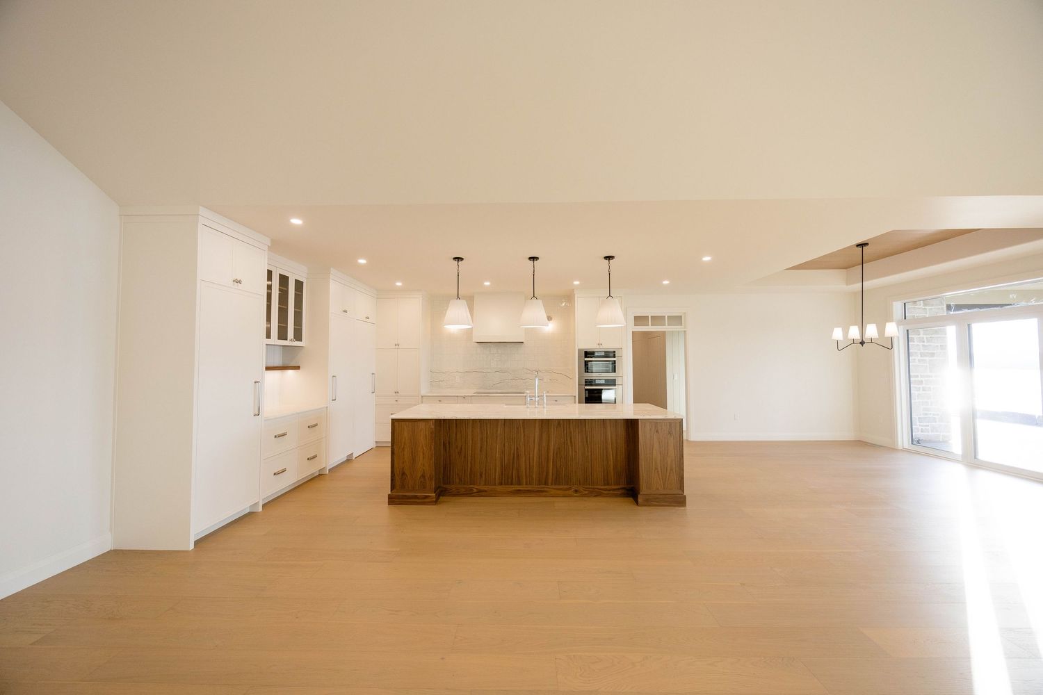 Spacious open-plan kitchen featuring walnut island, white cabinets, pendant lighting, and wide-plank hardwood floors.