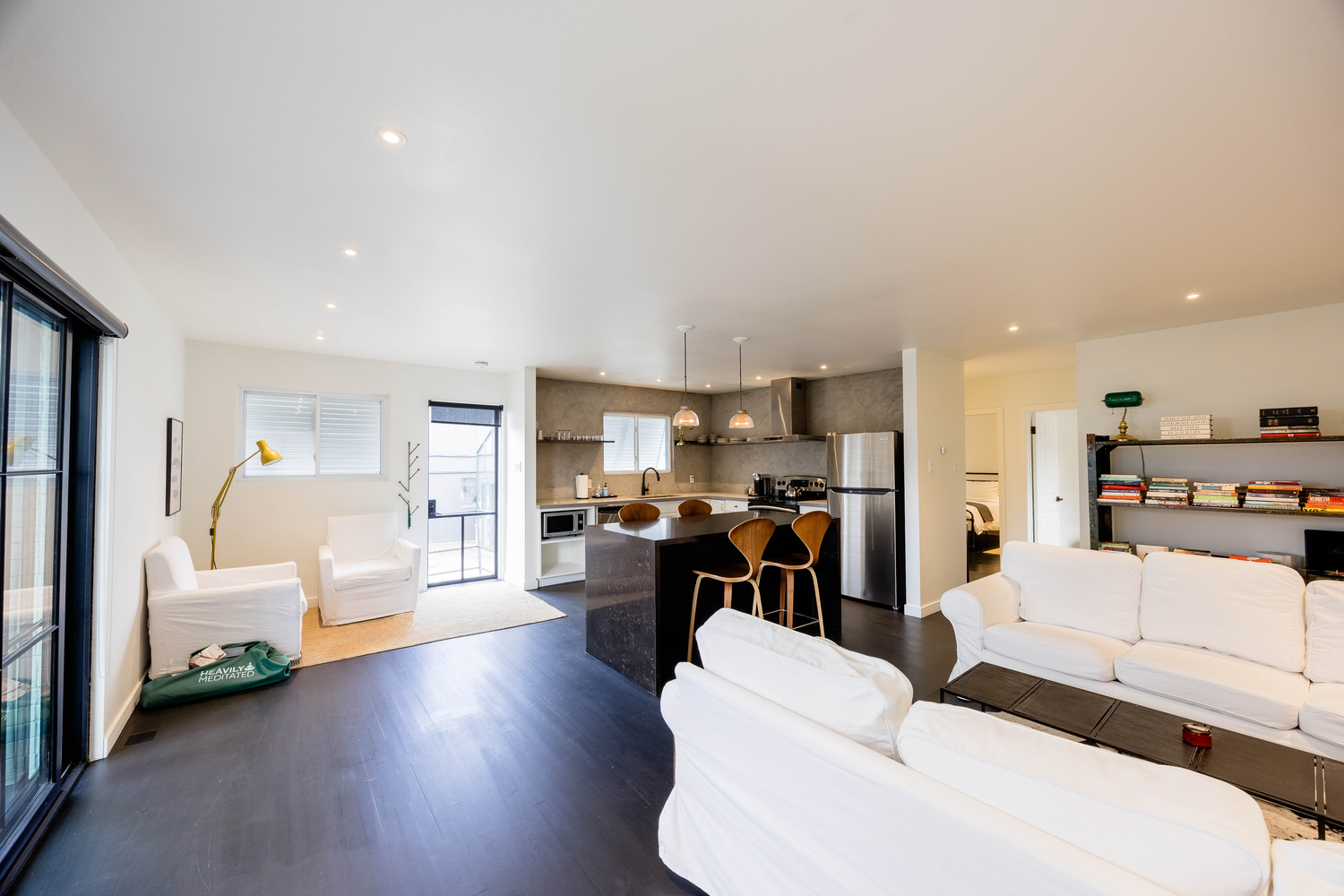 Open-plan living room with white sofas, dark hardwood floors, and modern kitchen in background.