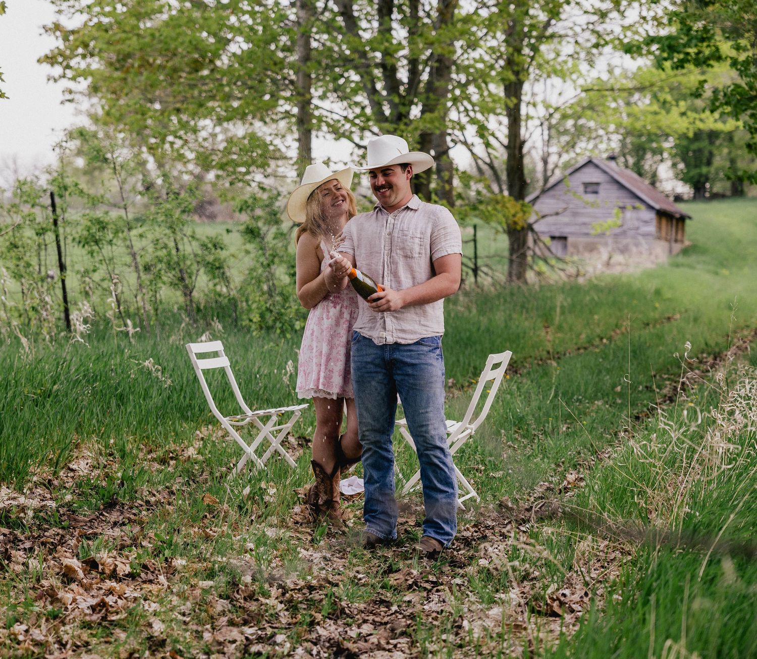 Couple sharing a romantic moment in a rustic countryside setting with white garden chairs.