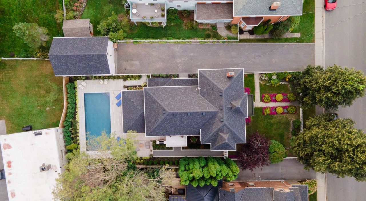 Aerial view of residential home with pool, gray roof, and manicured landscaping in suburban neighborhood.