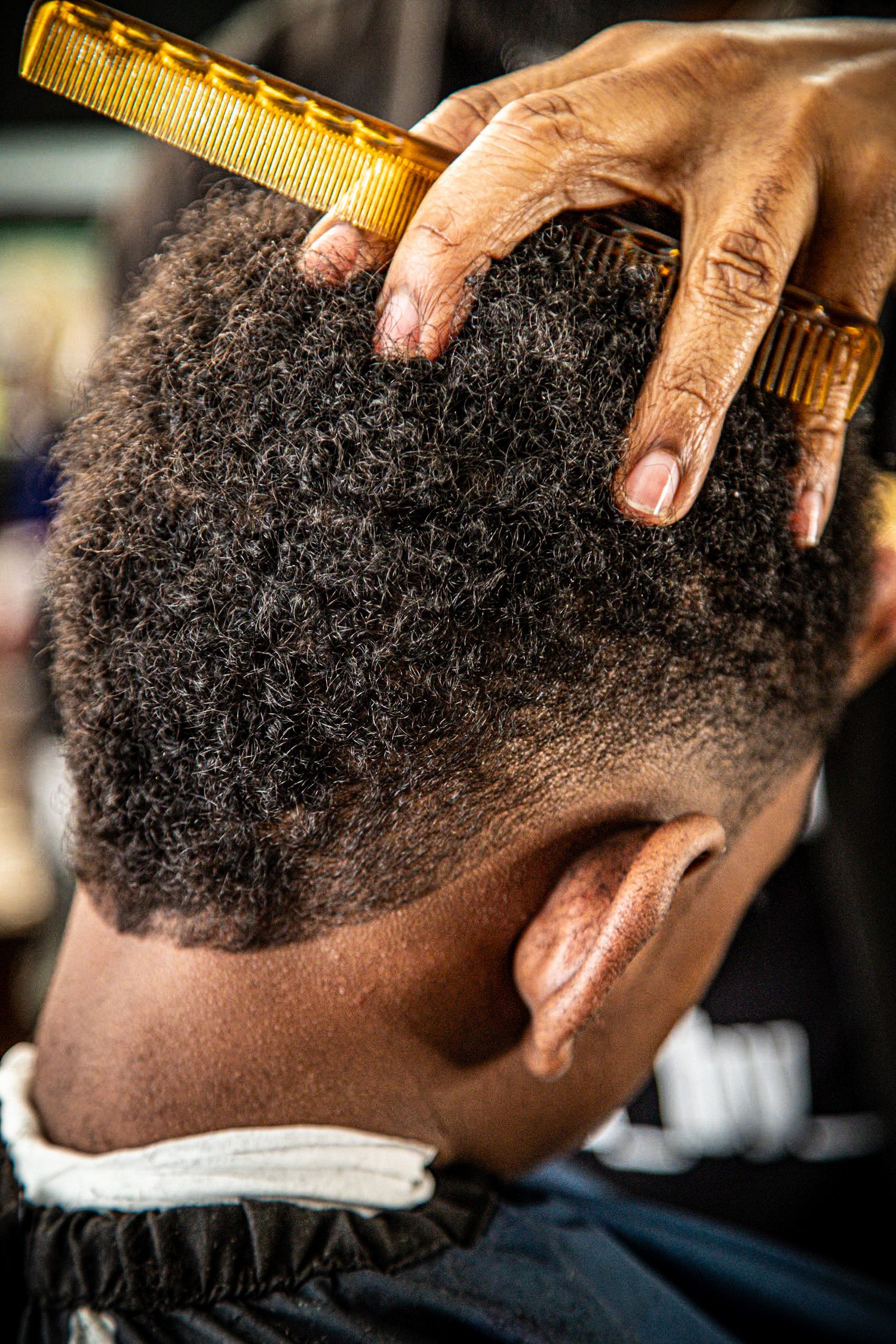 Close-up of a barbers hand combing through a clients natural curly hair.