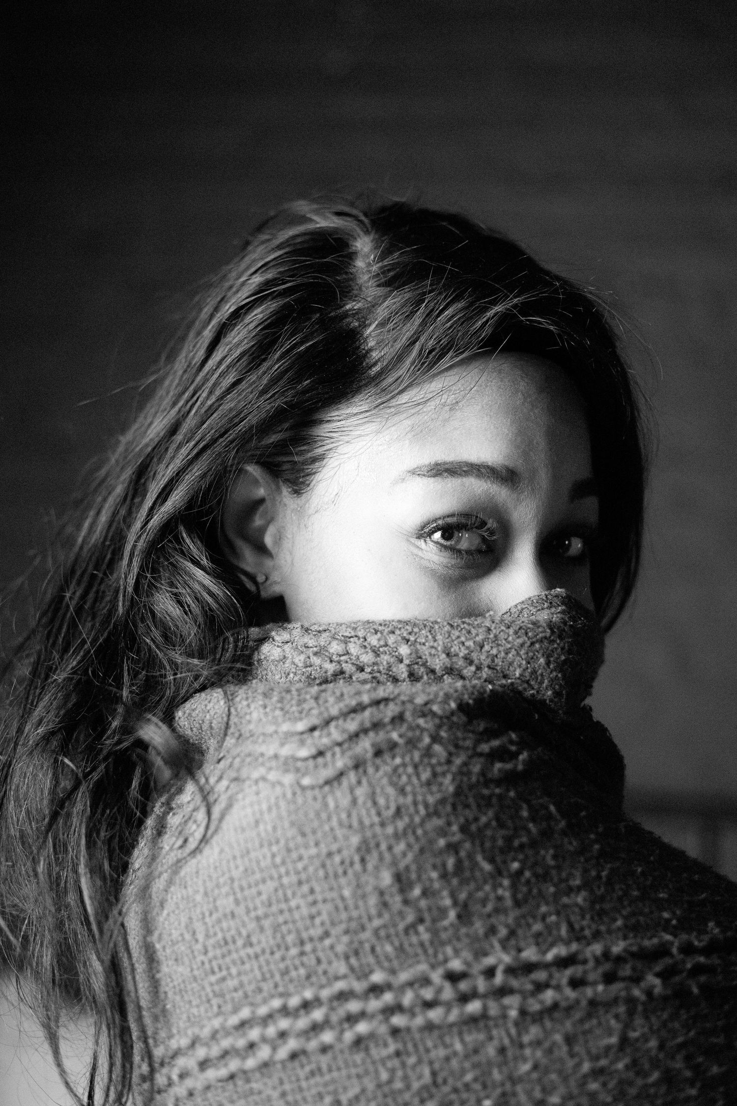Black and white close-up portrait of a woman hiding her face in a knit sweater.