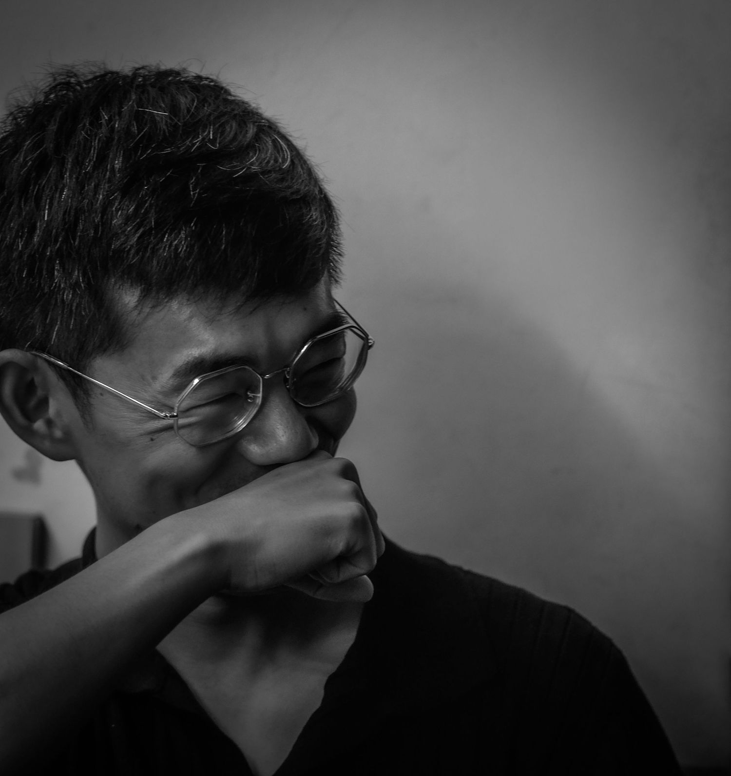 Black and white portrait of smiling Asian man with glasses resting chin on hand.
