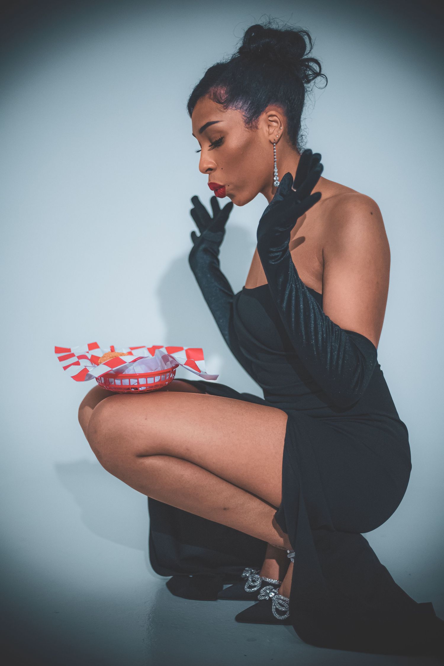Elegant woman in black dress and gloves crouching while examining a red and white gift box.