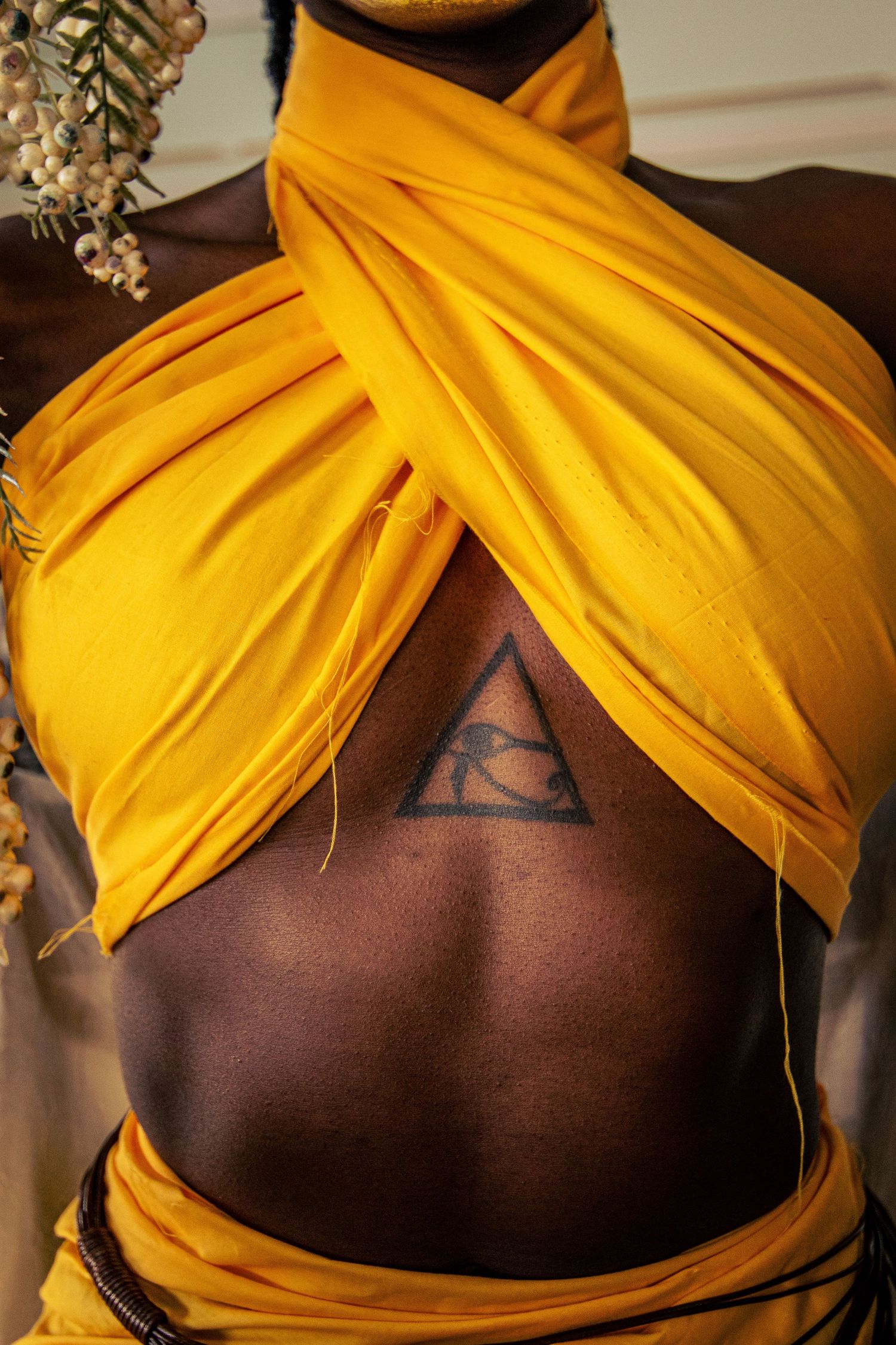 Close-up of an Eye of Horus tattoo on chest with golden yellow draped fabric costume and floral accessory.