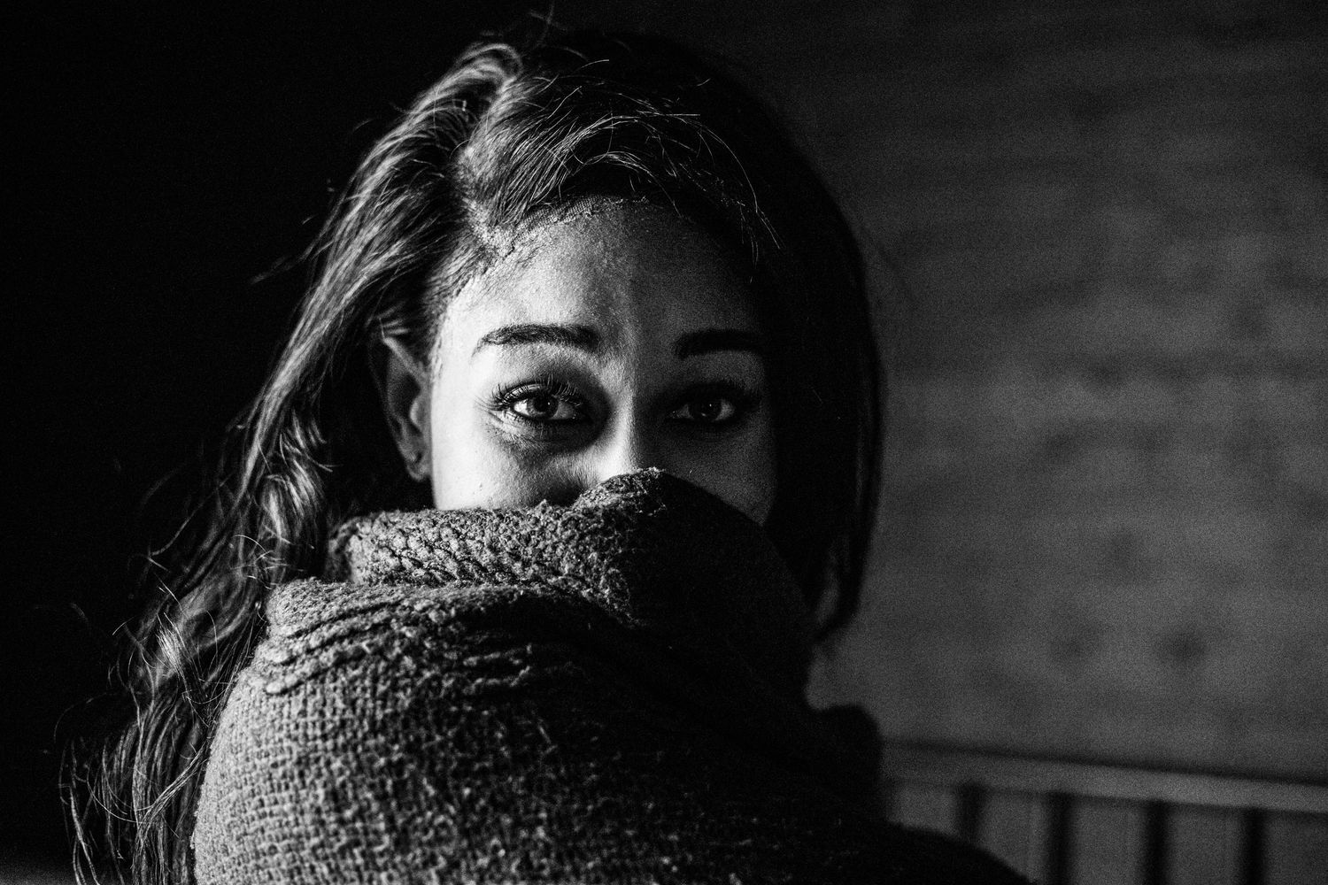 Dramatic black and white portrait of a woman with dark hair hiding her face behind a knit sweater.