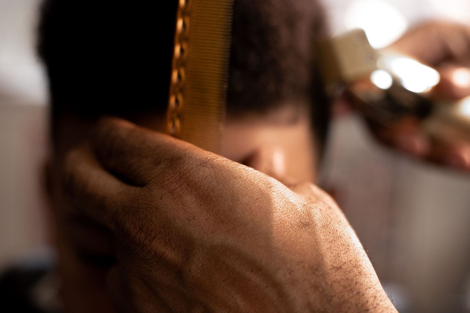 Close-up of a barber's weathered hand holding a comb through a client's dark curly hair.