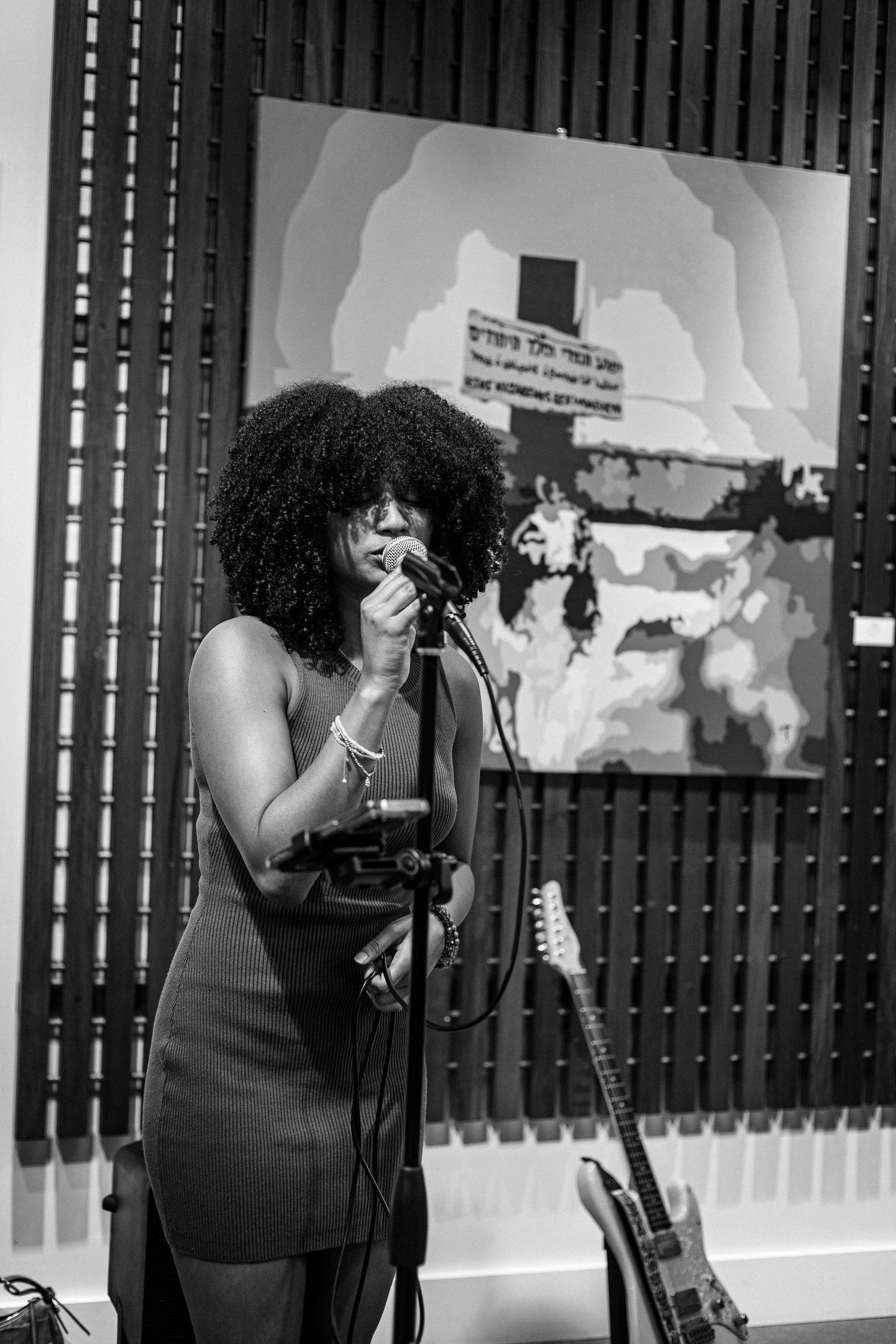 Black and white close-up of curly-haired woman singing into microphone at music event.