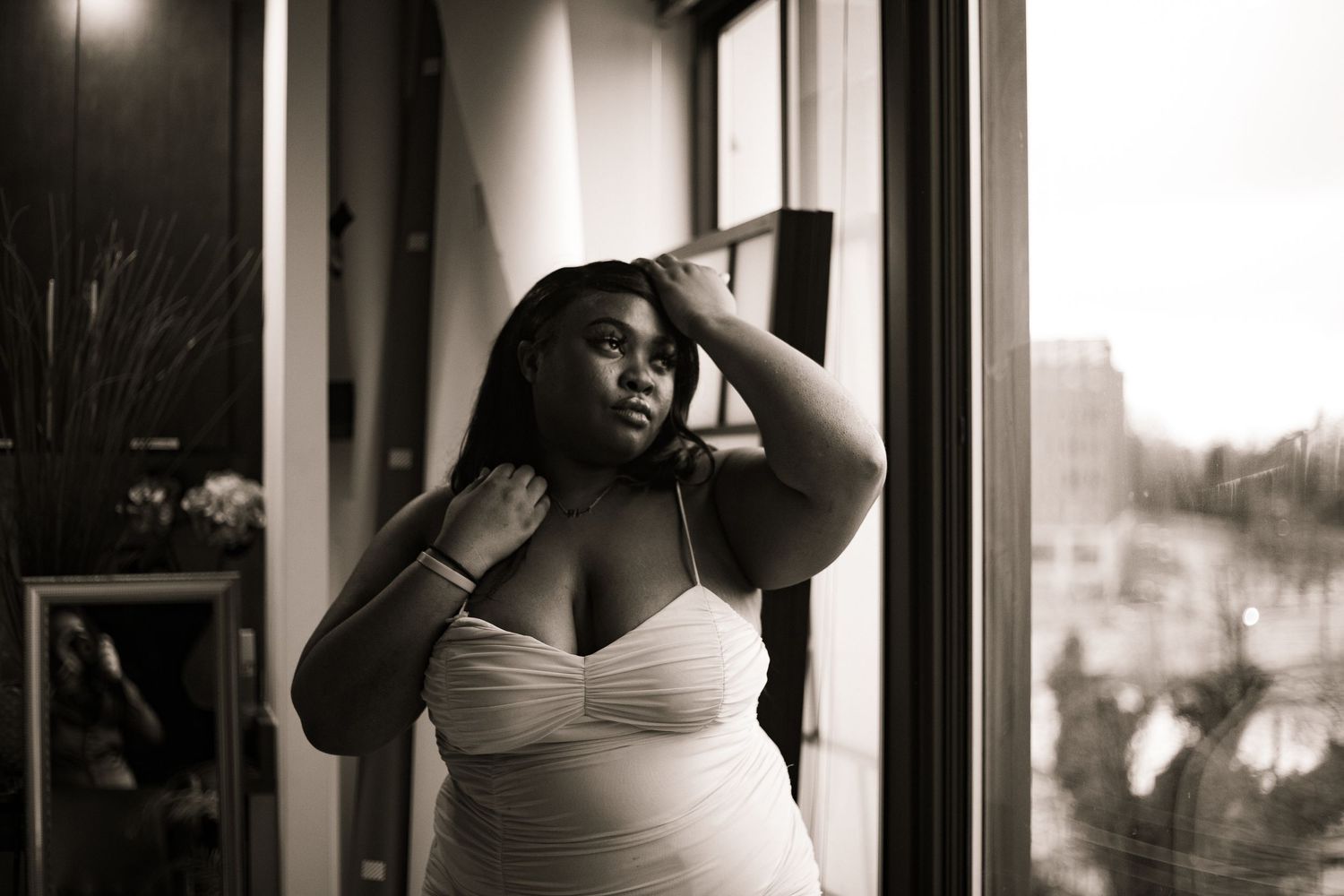Vintage-style black and white photo of a plus-size woman in white dress by window.