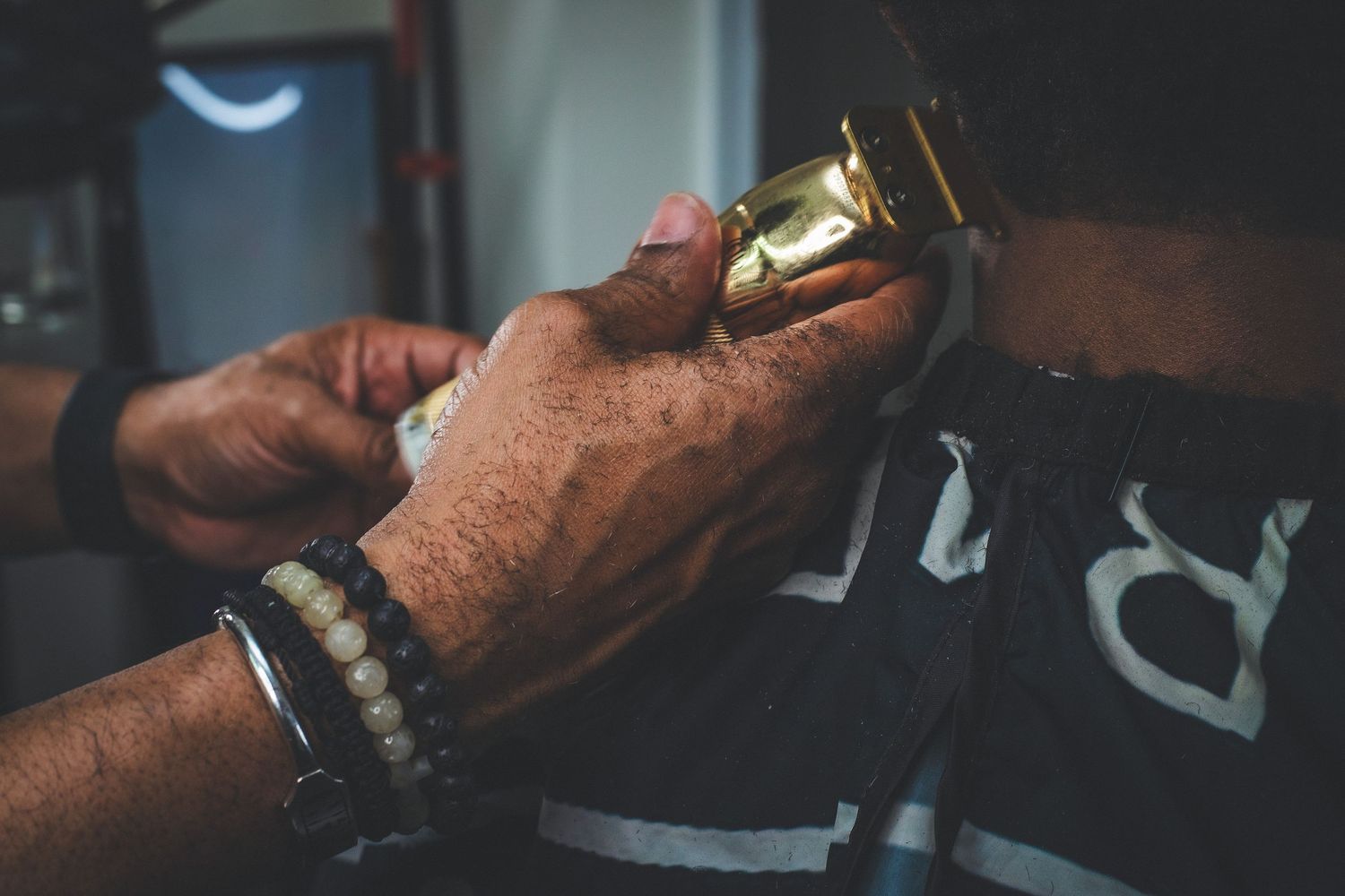 Close-up of barber hands using gold hair clippers on a client in a barbershop.