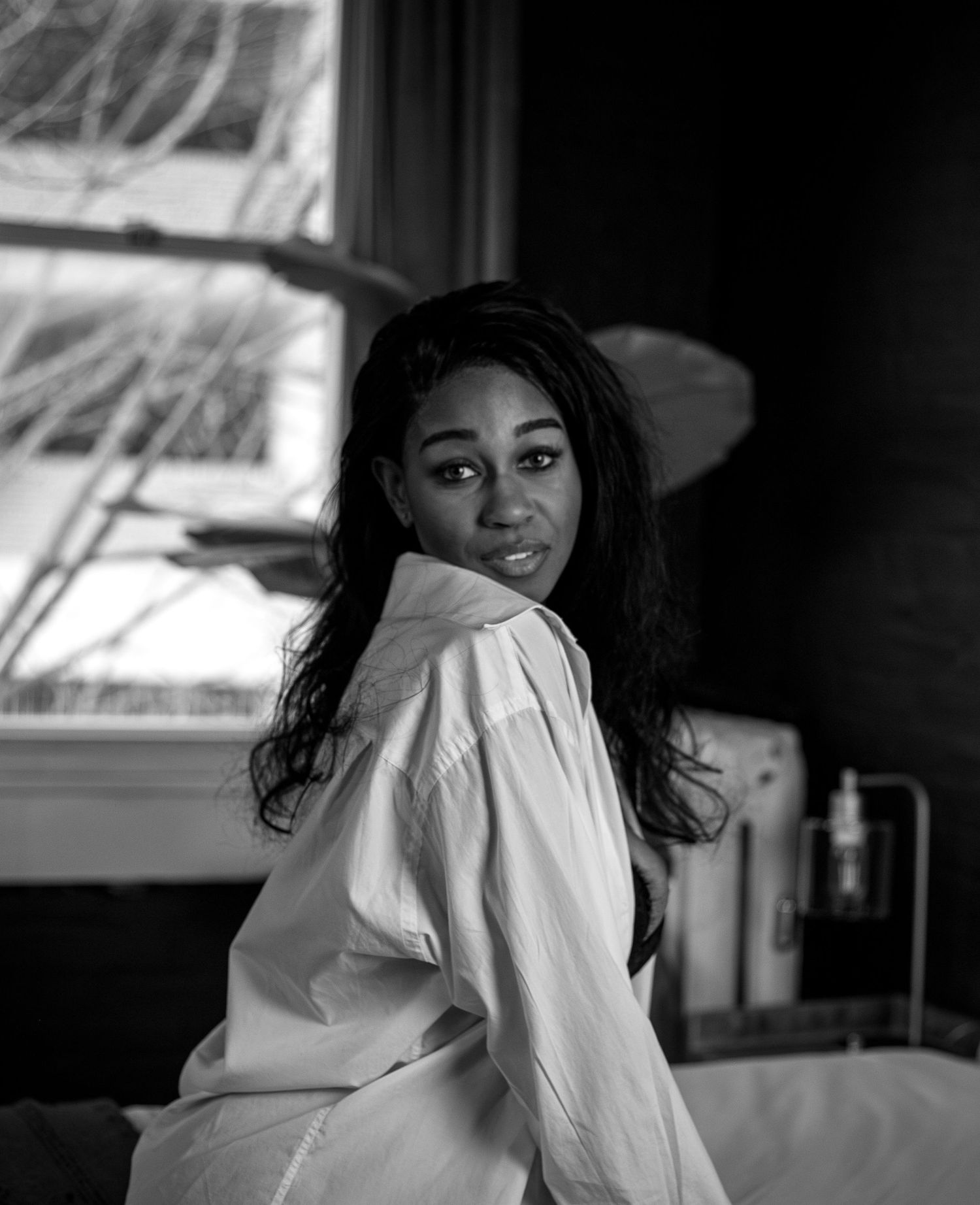 Black and white portrait of a woman in a white shirt sitting near a window.