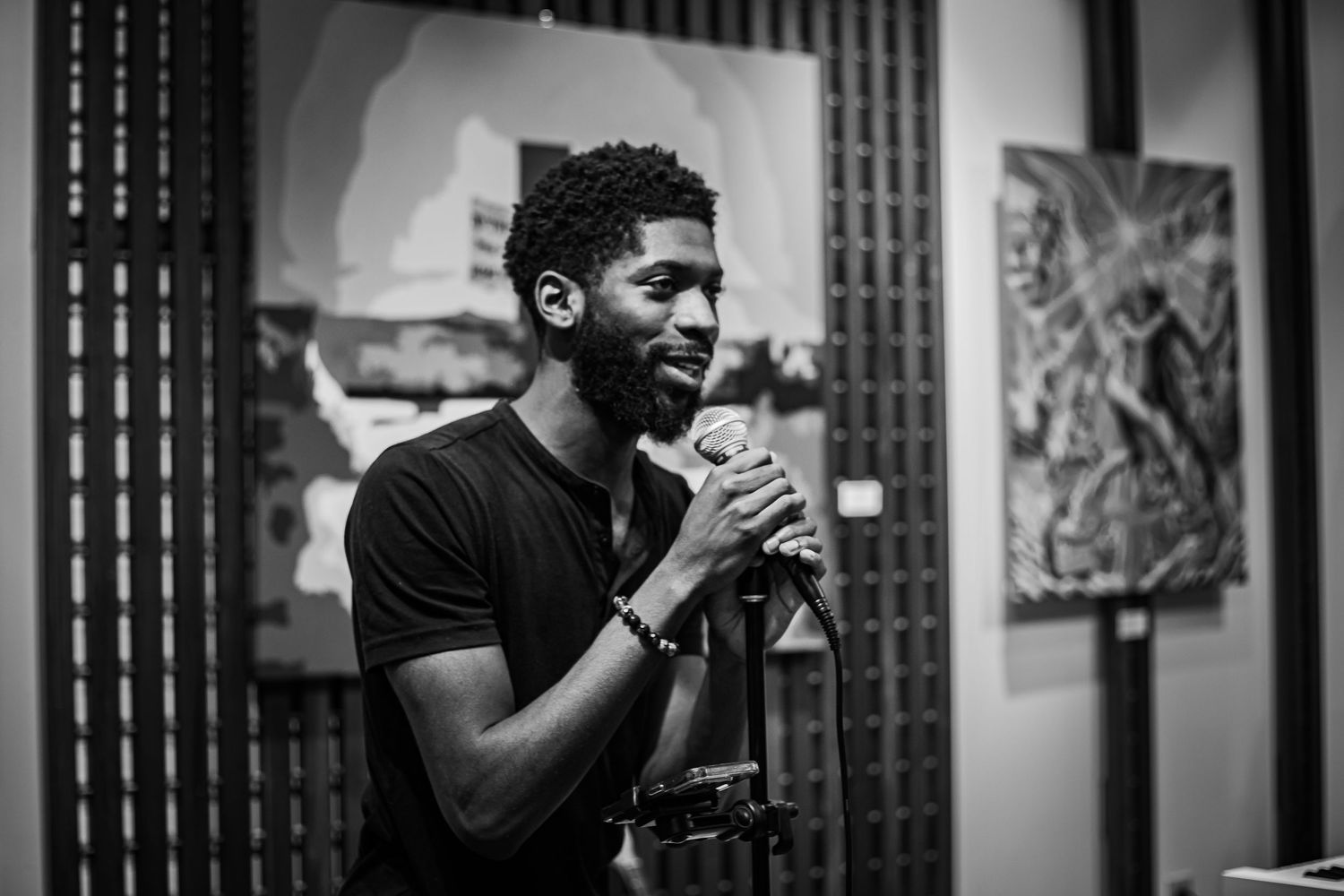 Black and white portrait of a man singing into a microphone at an art gallery event.
