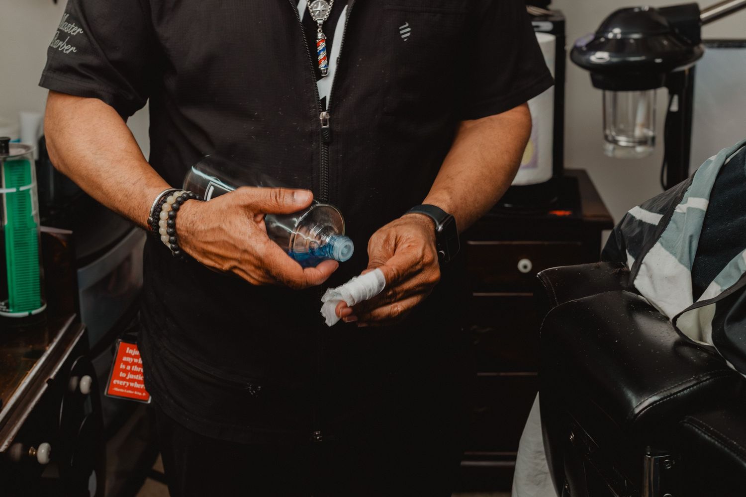 Barber in black uniform preparing hair care products at a barbershop station.