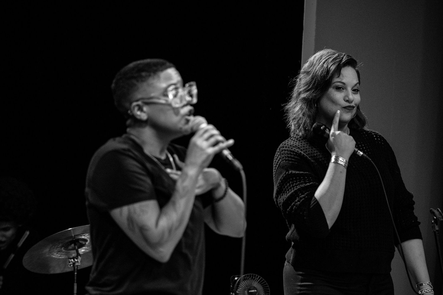 Black and white image of male and female vocalists performing together on stage.
