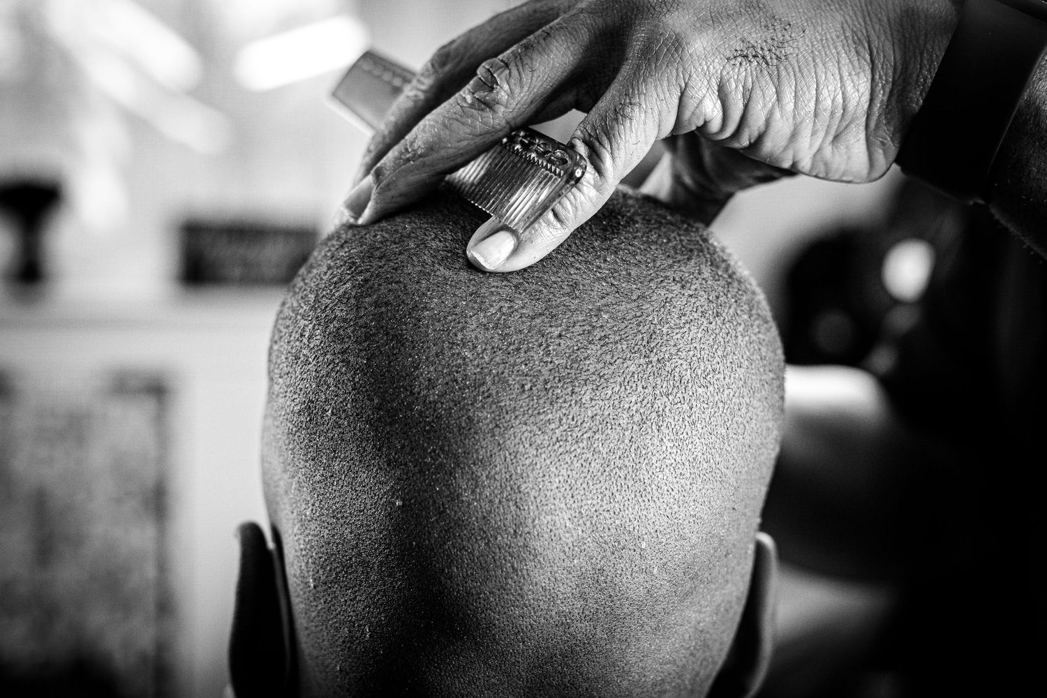 Black and white close-up of a barber using clippers to shave a clients head.