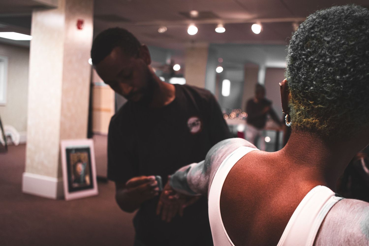 Candid photo of two people in a gallery space, one applying body paint to the other's arm.