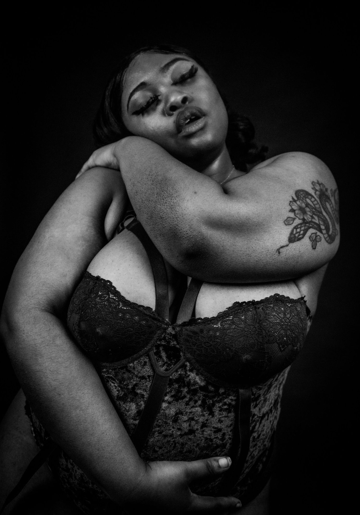 Black and white boudoir portrait of a plus-size woman in velvet and lace bra with floral tattoo.