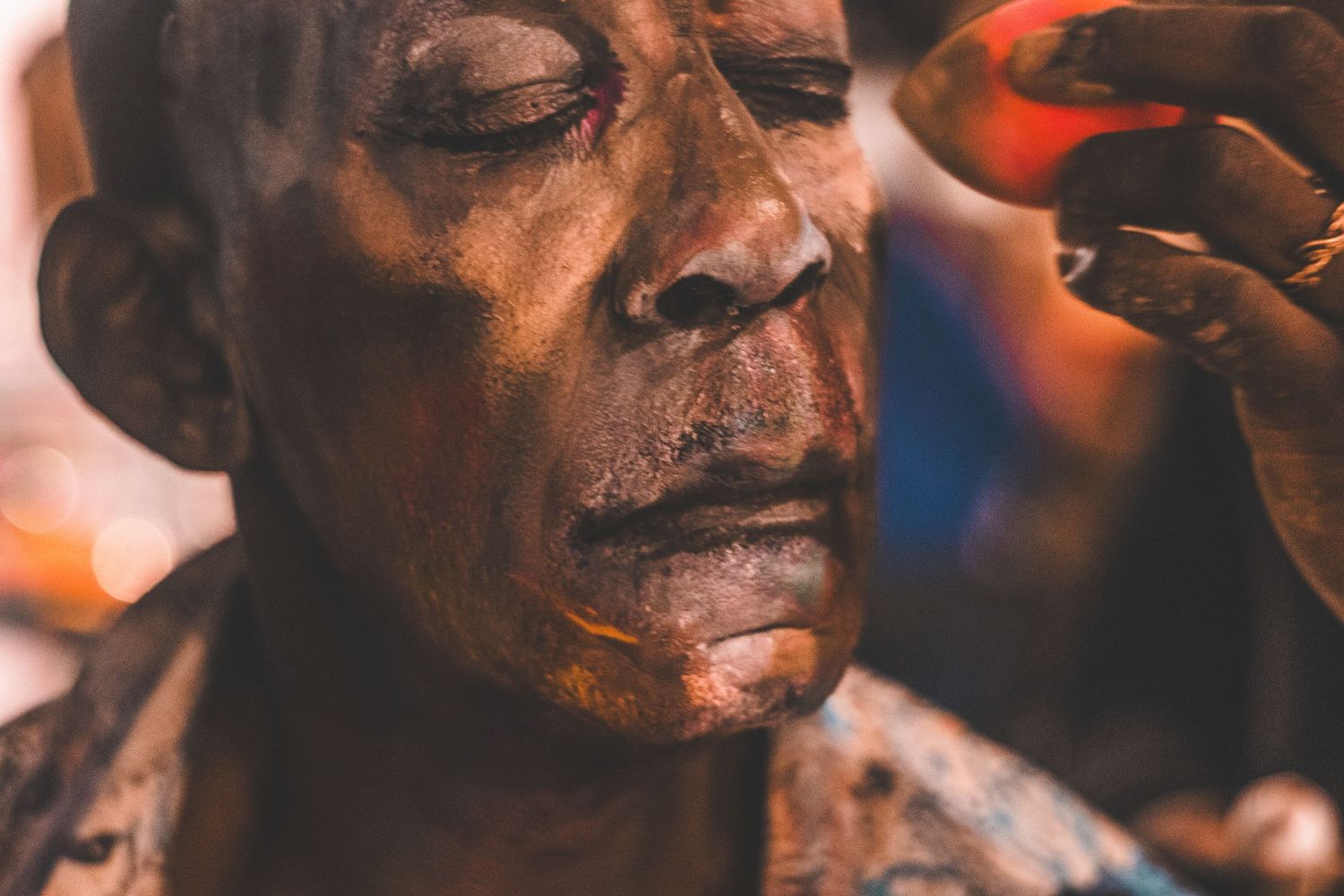 Artist carefully applies dark brown body paint to a mans face in a detailed close-up shot.