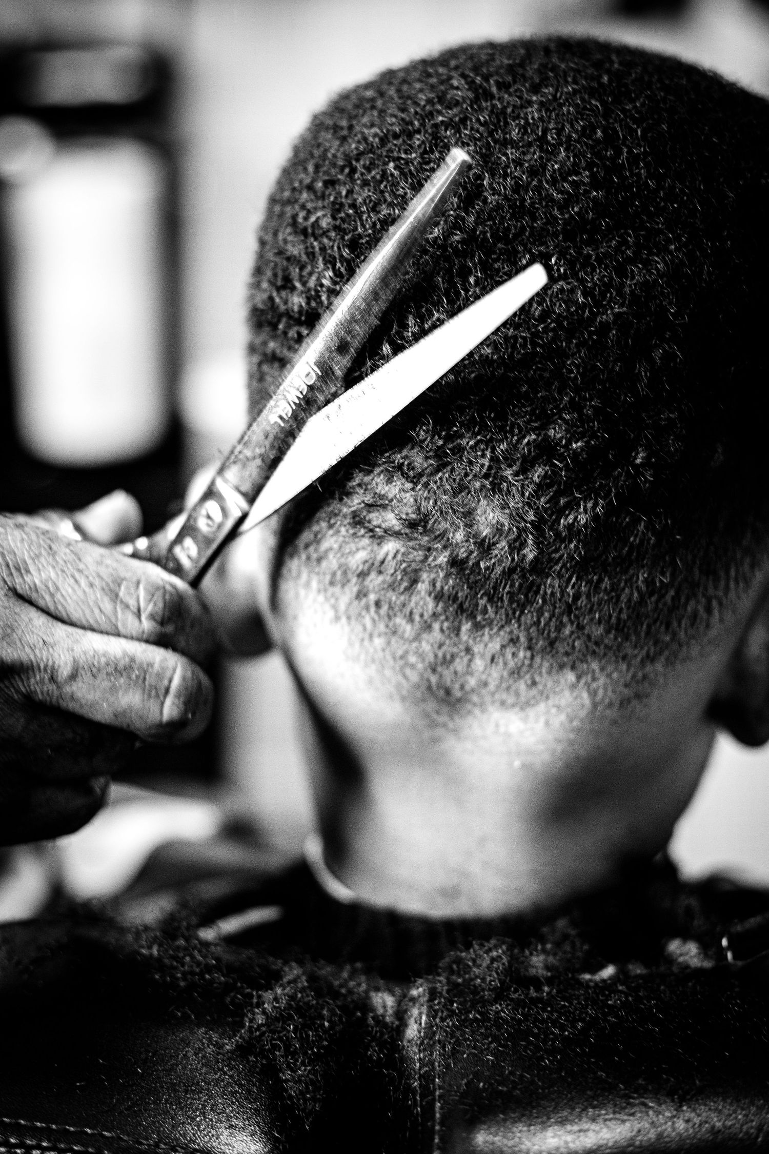 Black and white close-up of barber cutting hair with scissors in a barbershop.