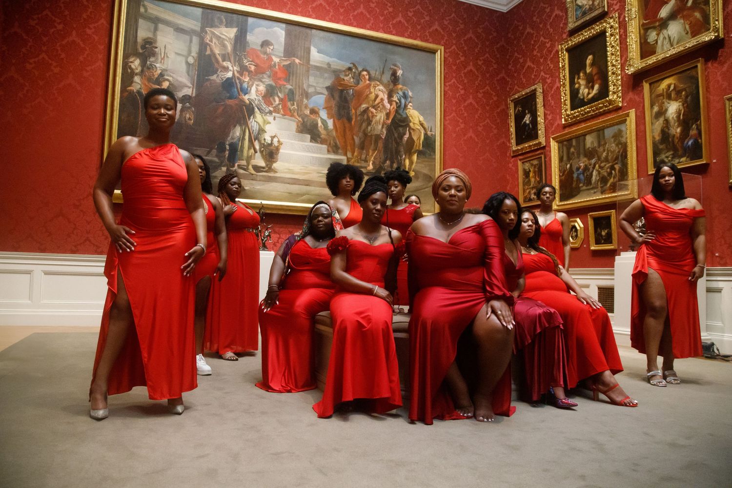Group of women in red gowns posing in art gallery room.