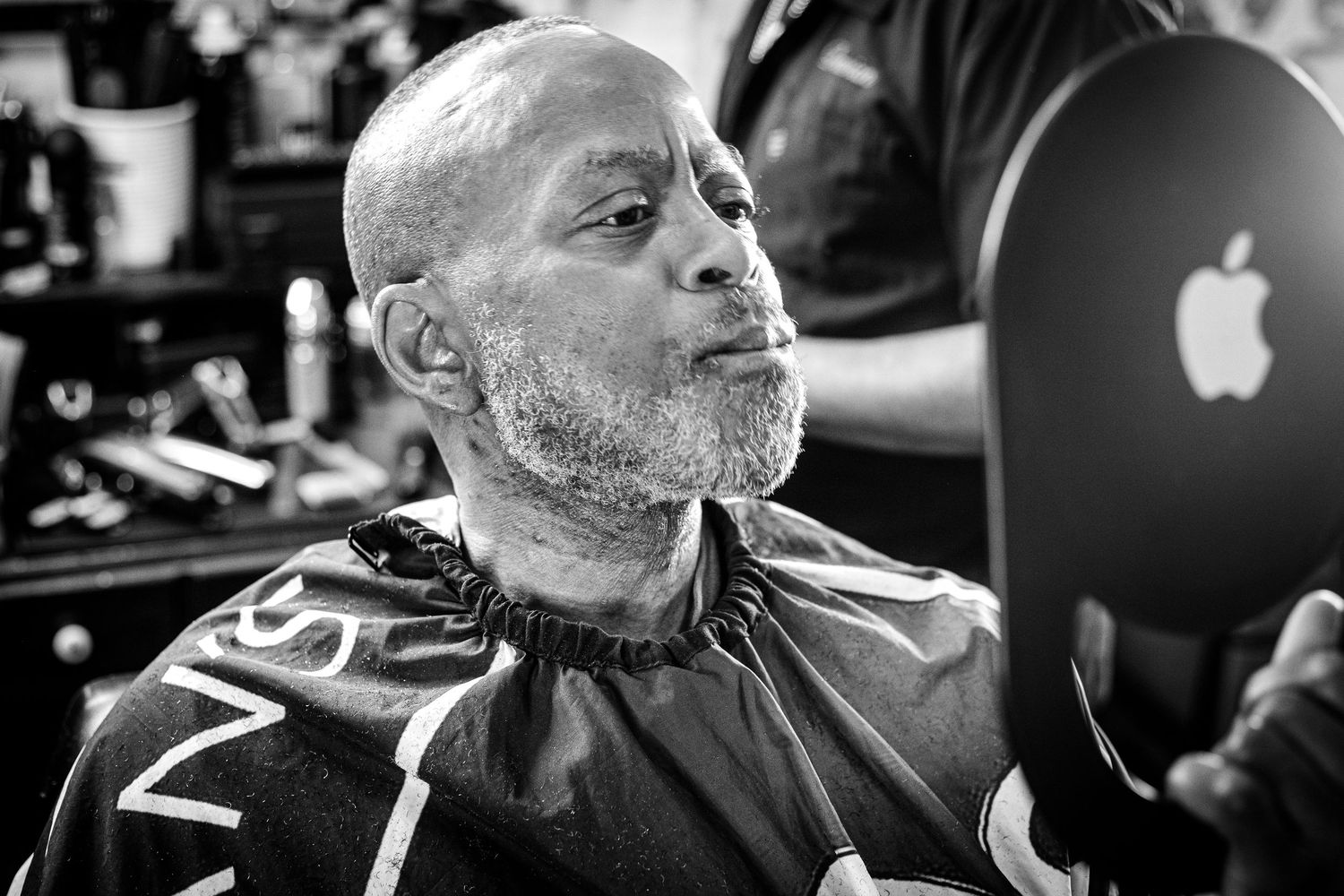 Black and white portrait of a bald man with a beard sitting in a barber chair.