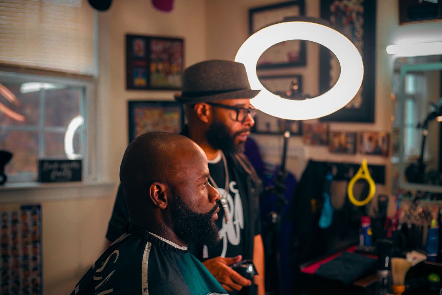 Barber styling a clients hair under a ring light in a vibrant barbershop.