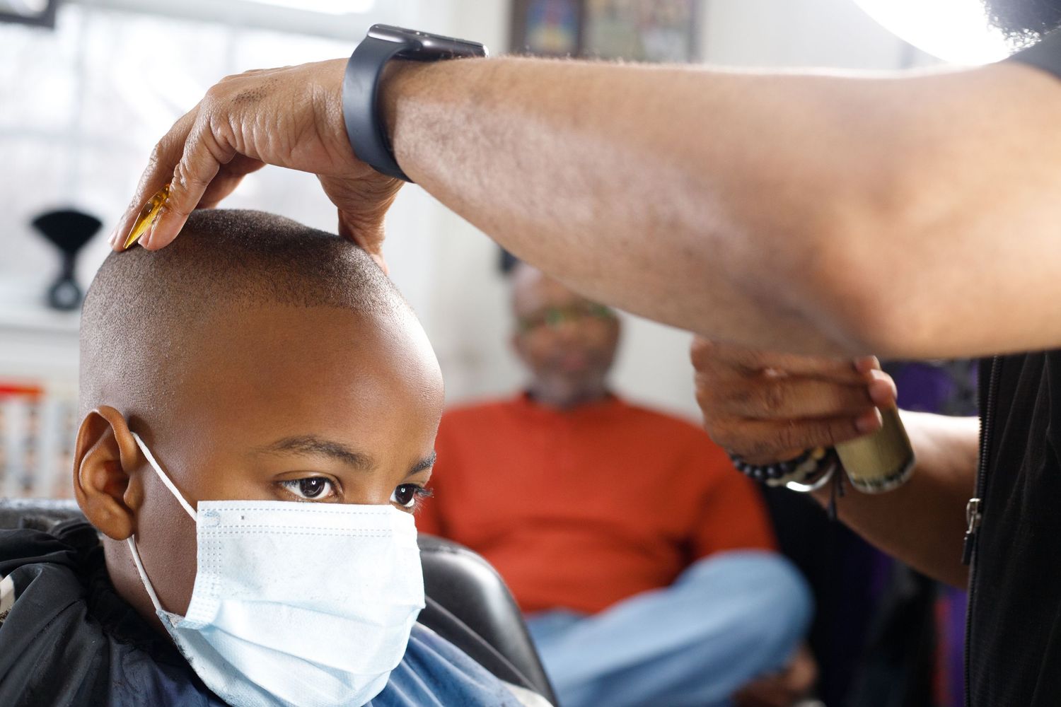 Young boy wearing a face mask getting a haircut at a barbershop while sitting in a chair.