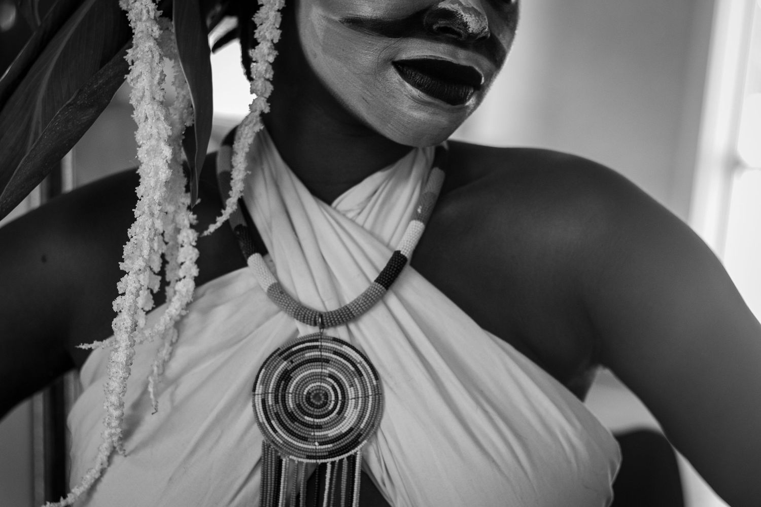 Black and white close-up of a woman in a white halter top wearing a large spiral pendant necklace smiling.
