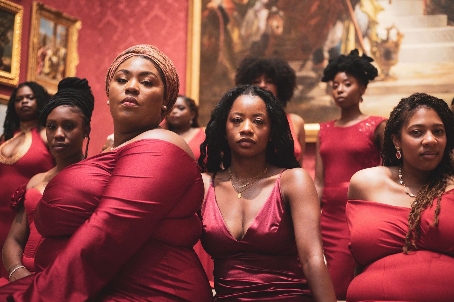 Women in red dresses posing in front of classic paintings.